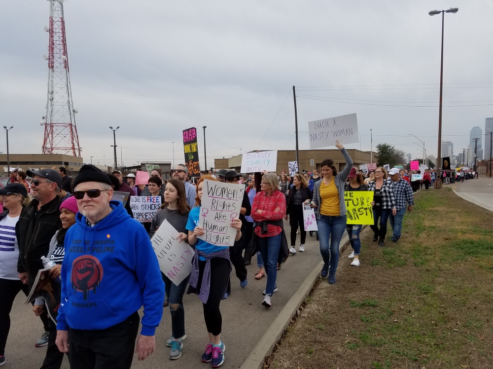 Marchers walking with downtown Dallas in the background. 